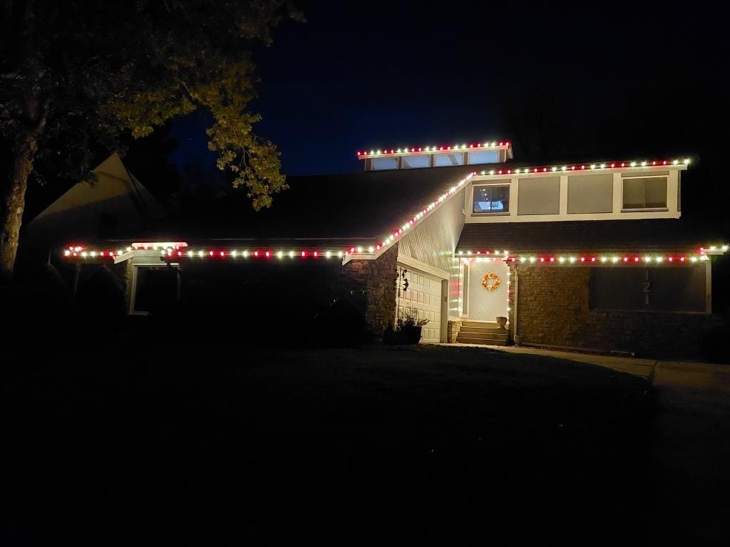 Split-level home with alternating red and white Christmas lights and a lit wreath on the front door